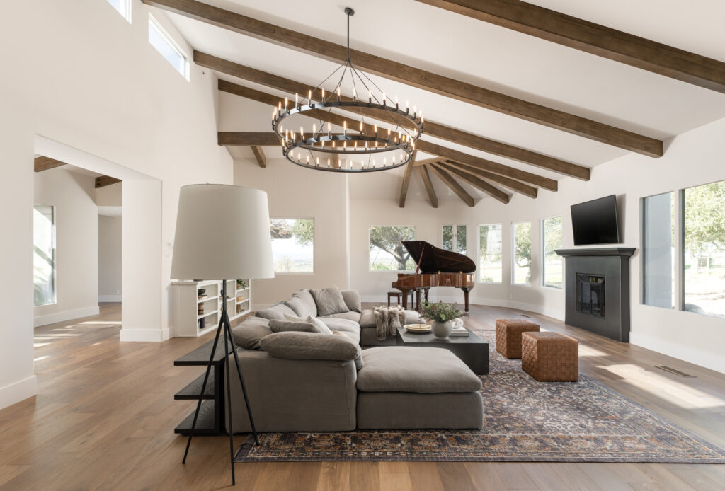 formal living room in santa ynez luxury home with restoration hardware cloud modular sectional, baby grand piano, restoration hardware camino vintage filament two-tier chandelier, loloi rosemary rug in gray, and Studio Mcgee for target ottoman, black fireplace, built-in