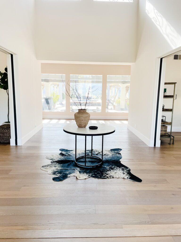 Entry to Santa Ynez luxury home round marble table with black base cowhide rug vintage vase with large branches and soapstone catchall