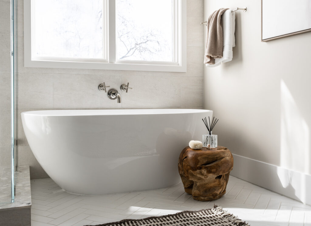 Sleek freestanding tub with round, tapered sides. It has a Kohler Purist wall mount tub filler in polished nickel and the surround is finished with limstone tile.