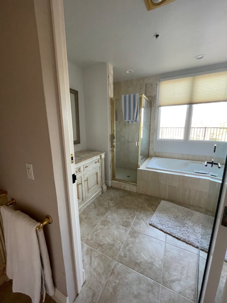 These are the before photos of an ensuite bathroom in a luxury home. Designed in the 90s it is a tuscan style with faux travertine porcelain tile and shiny gold hardware. The tub has a tile surround.